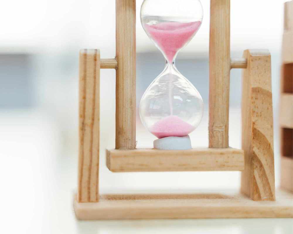 Image of a sand timer with pink sand. It's sitting on a white bench